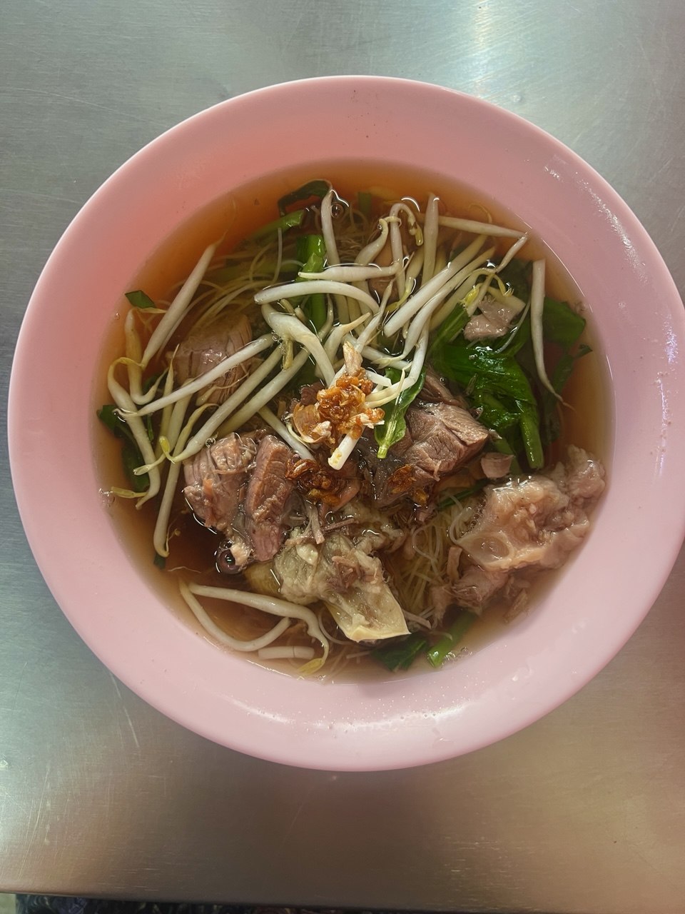 bowl of clear-broth noodle soup with beef, bone-in meat, bean sprouts, and greens