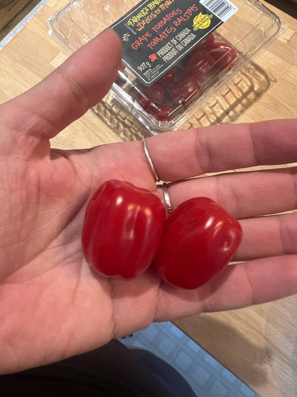 two grape tomatoes shown in hand with package labeled grape tomatoes in the background