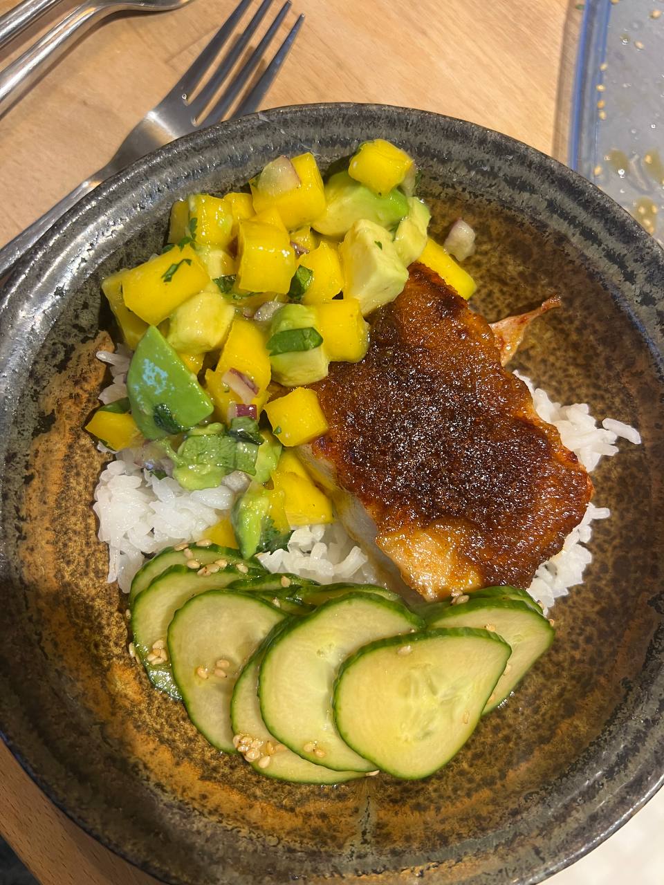bowl with white rice, salmon with brown sugar, paprika, garlic, and onion rub, mango-avocado salad with red onion, cilantro, and lemon juice, plus cucumber in soy-rice-vinegar sauce with sesame seeds