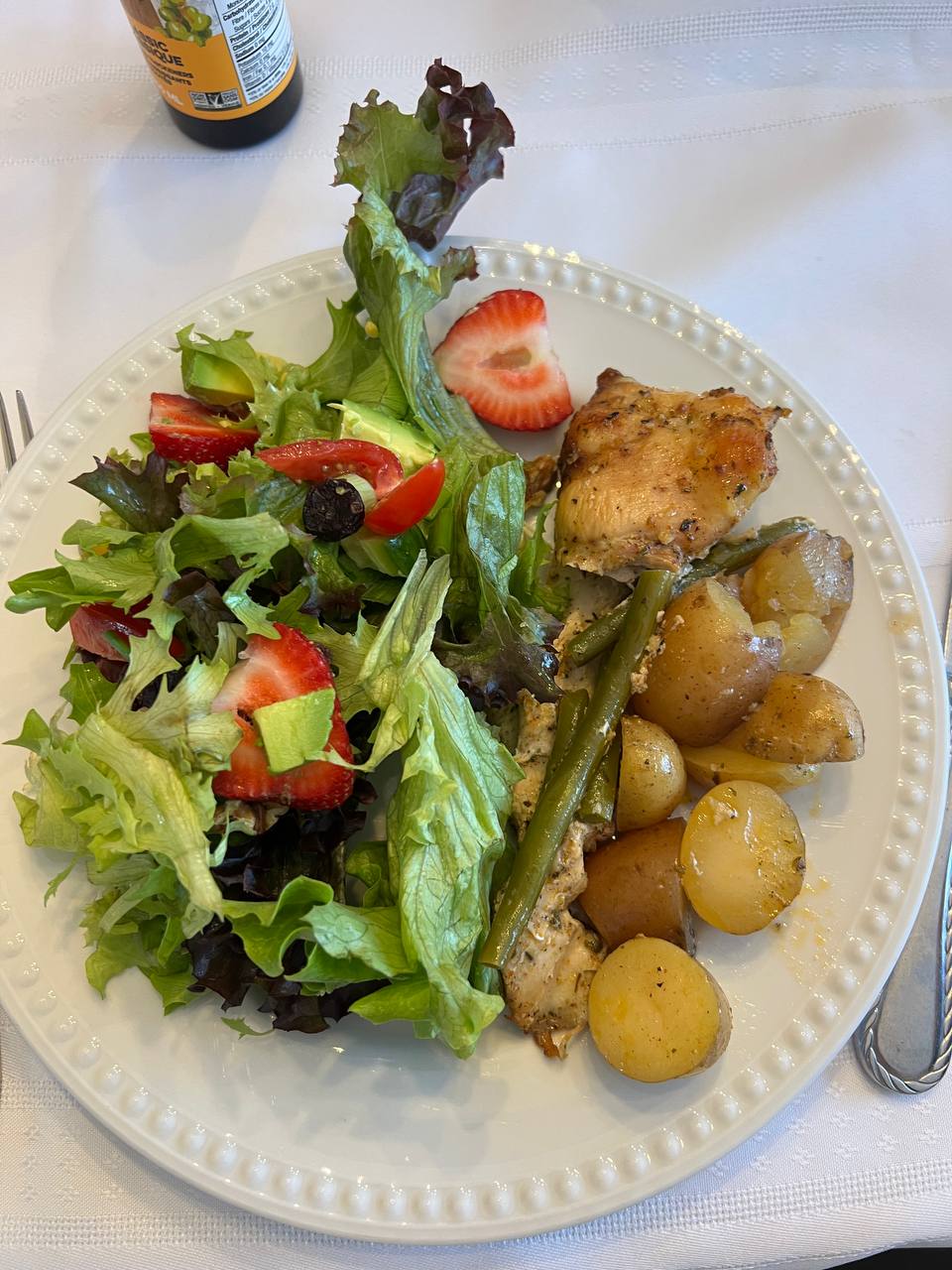 Baked/roasted chicken breast (approximately 3/4 of a breast), Baby potatoes (roasted or boiled, seasoned), Green beans (cooked, a few), Mixed green salad with avocado, strawberries, and cherry tomatoes