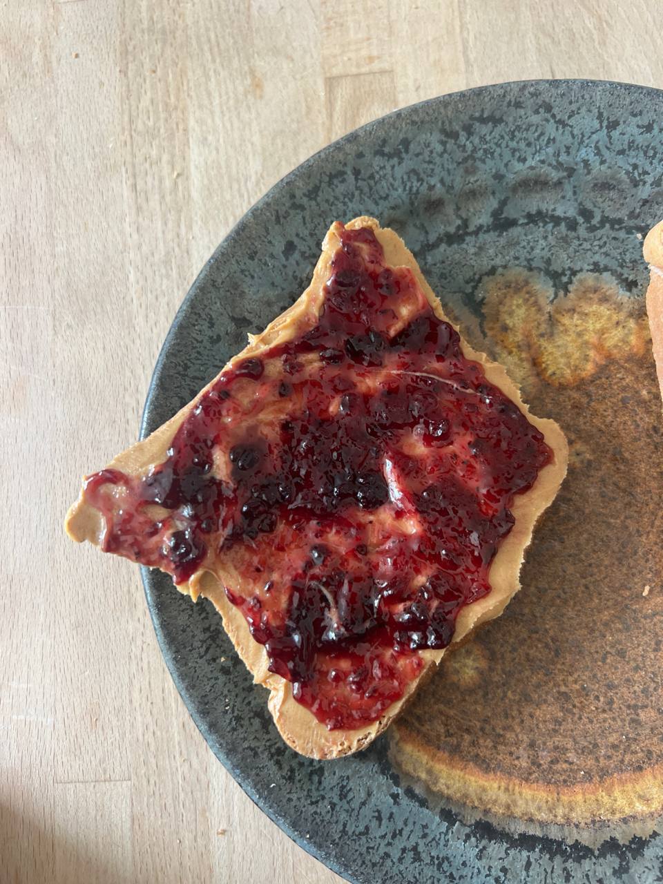 Slice of toast with peanut butter and berry jam (foreground, primary), Slice of plain toast (partially visible, background)