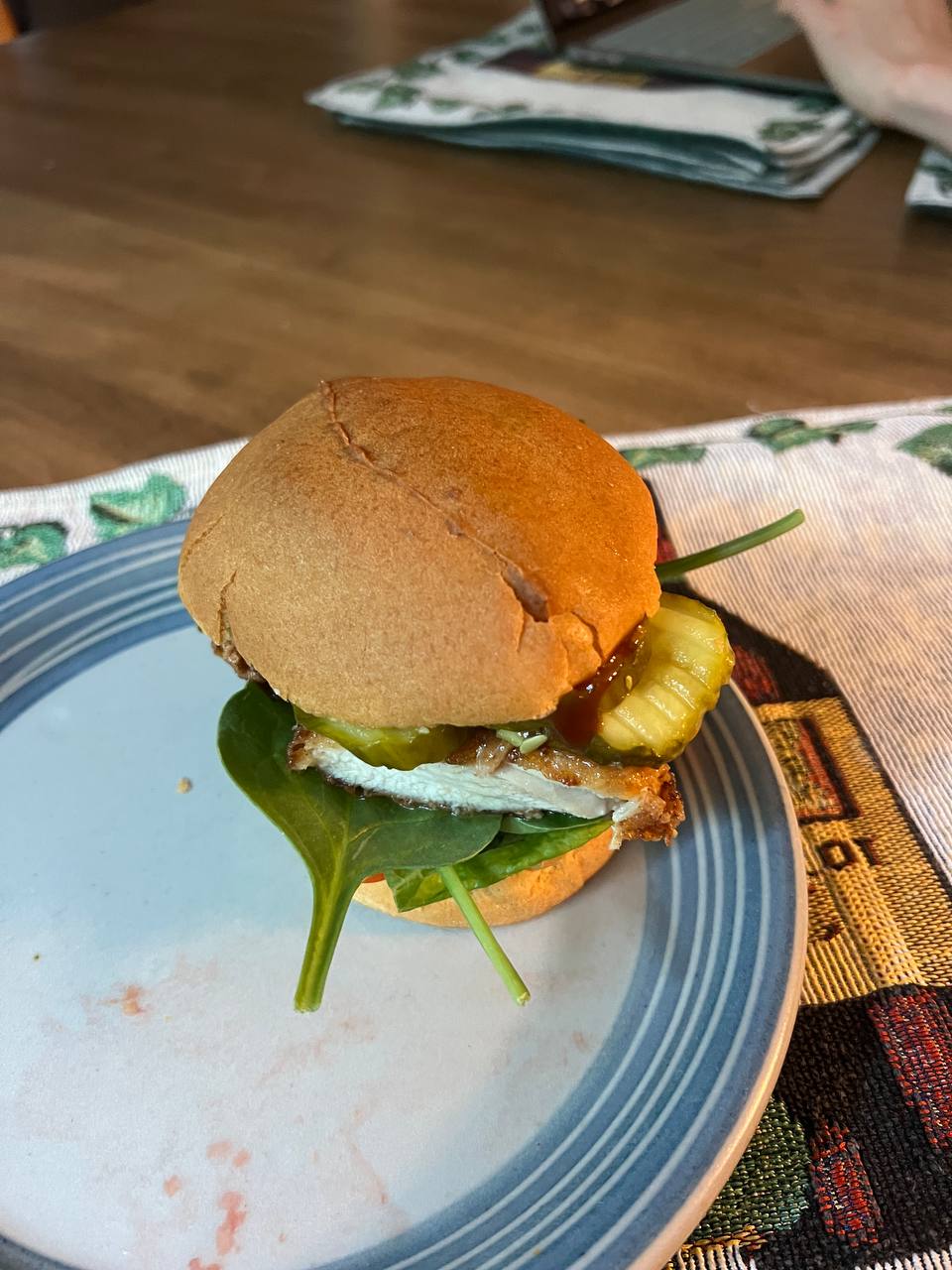 Chicken burger with breaded chicken patty, bun, spinach, tomato, pickles, and sauce